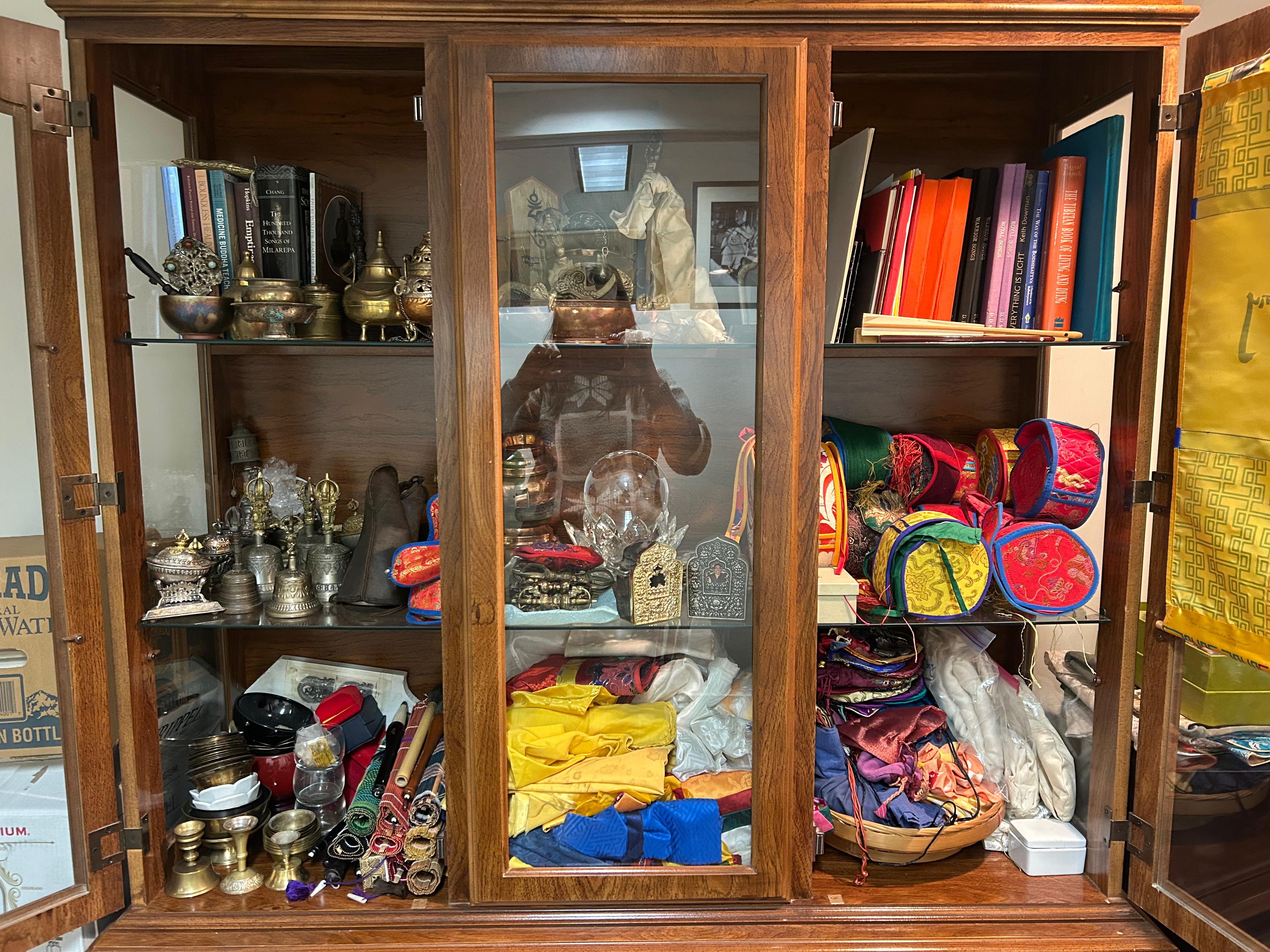 A wooden cabinet filled with donated ritual objects, bells, dorjes, brocade, and texts